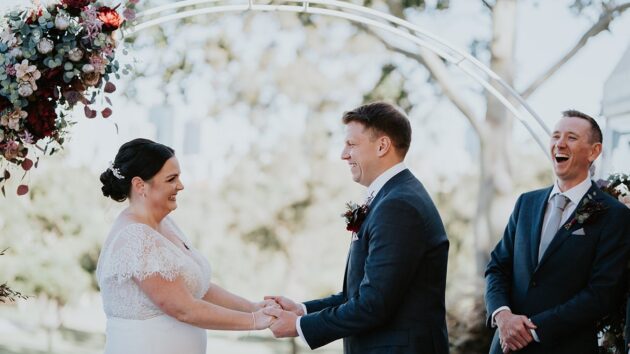 wedding ceremony with Brisbane City Celebrants full of fun laughter and love, with bride and groom and wedding party all smiling and laughing during the ceremony and native flowers on the wedding arbour