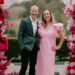 Preferred Wedding Celebrants of Victoria Park Jamie and Cara of Brisbane City Celebrants pictured with warm smiles at the Victoria Park Courtyard ceremony space. Jamie is wearing a teal jacket and white shirt and Cara is wearing a long pink dress with ruffled sleeves, and they are framed by vibrant wedding ceremony flowers