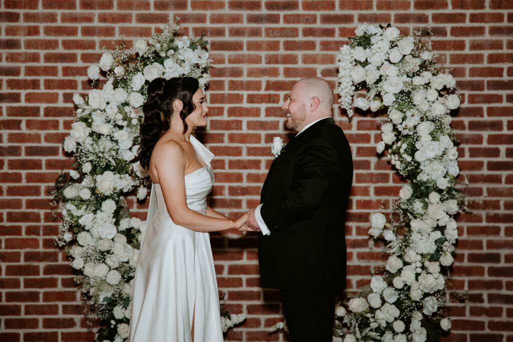 Celebrant Cara delivering an authentic wedding ceremony pictured bride and groom framed by white florals and a brick backdrop