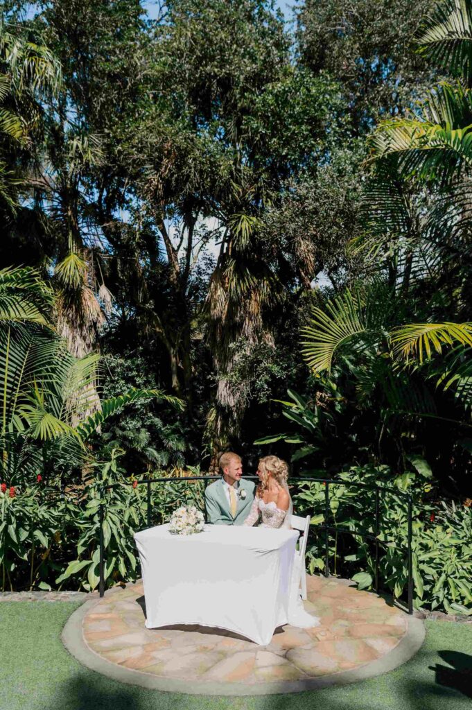 bride and groom at signing table to sign their marriage certifcates at Mt Coot-tha Botanical Gardens surrounded by lush greenery